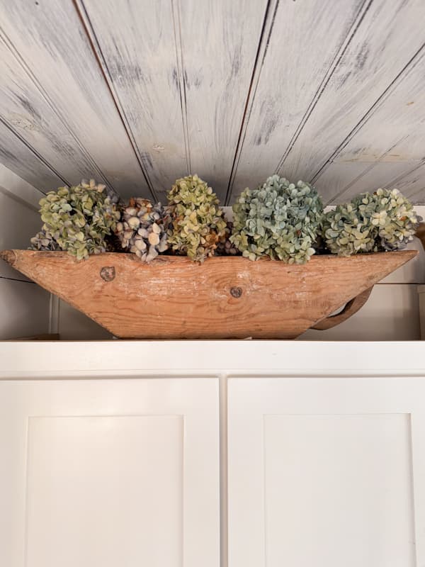 Antique dough filled with dried blue hydrangea blooms on top of kitchen cabinets.